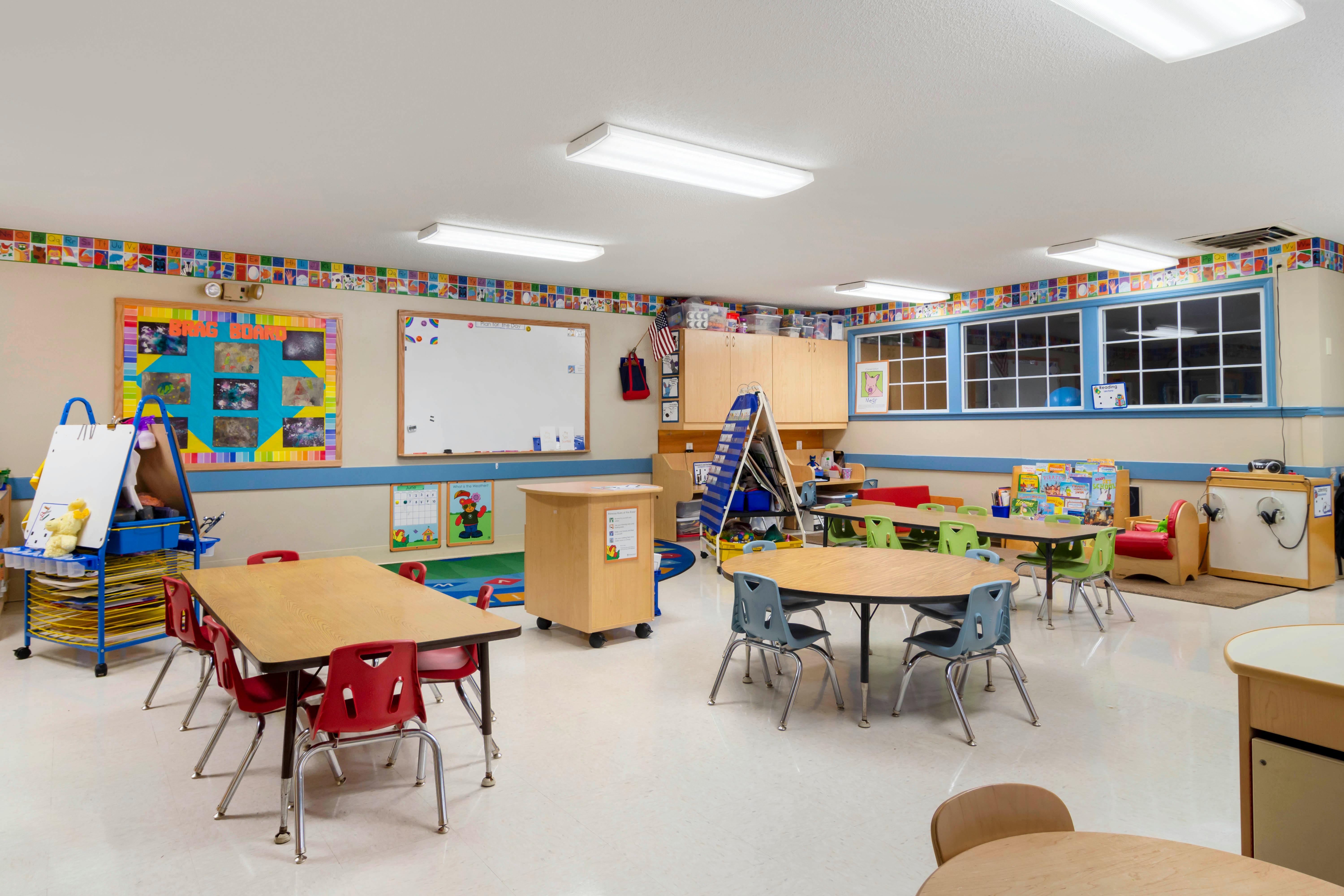 Empty classroom with tables and chairs for children, whiteboard, and learning displays