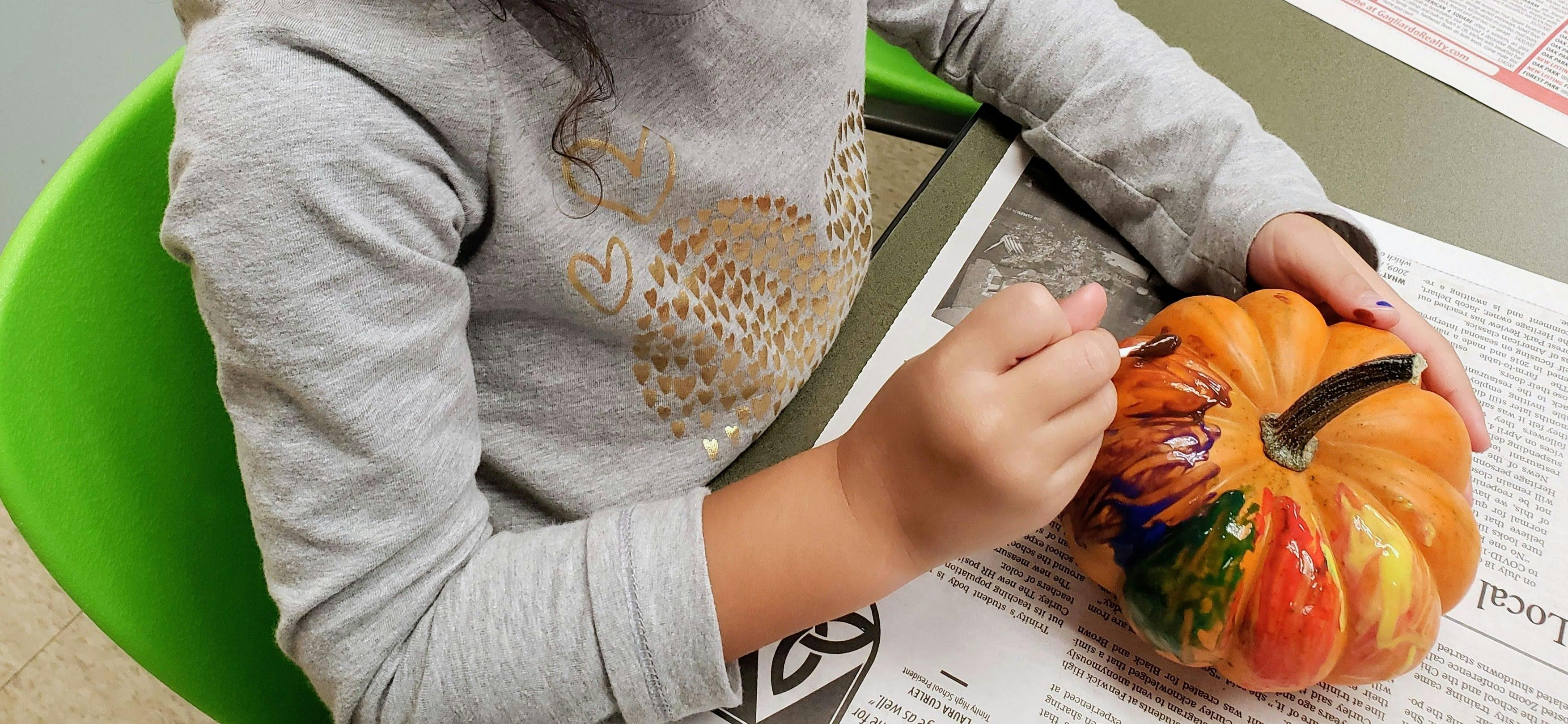 Child painting a small pumpkin on a table covered in newspaper