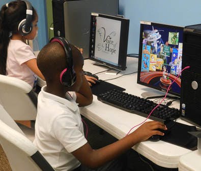 Two children wearing headphones using computers