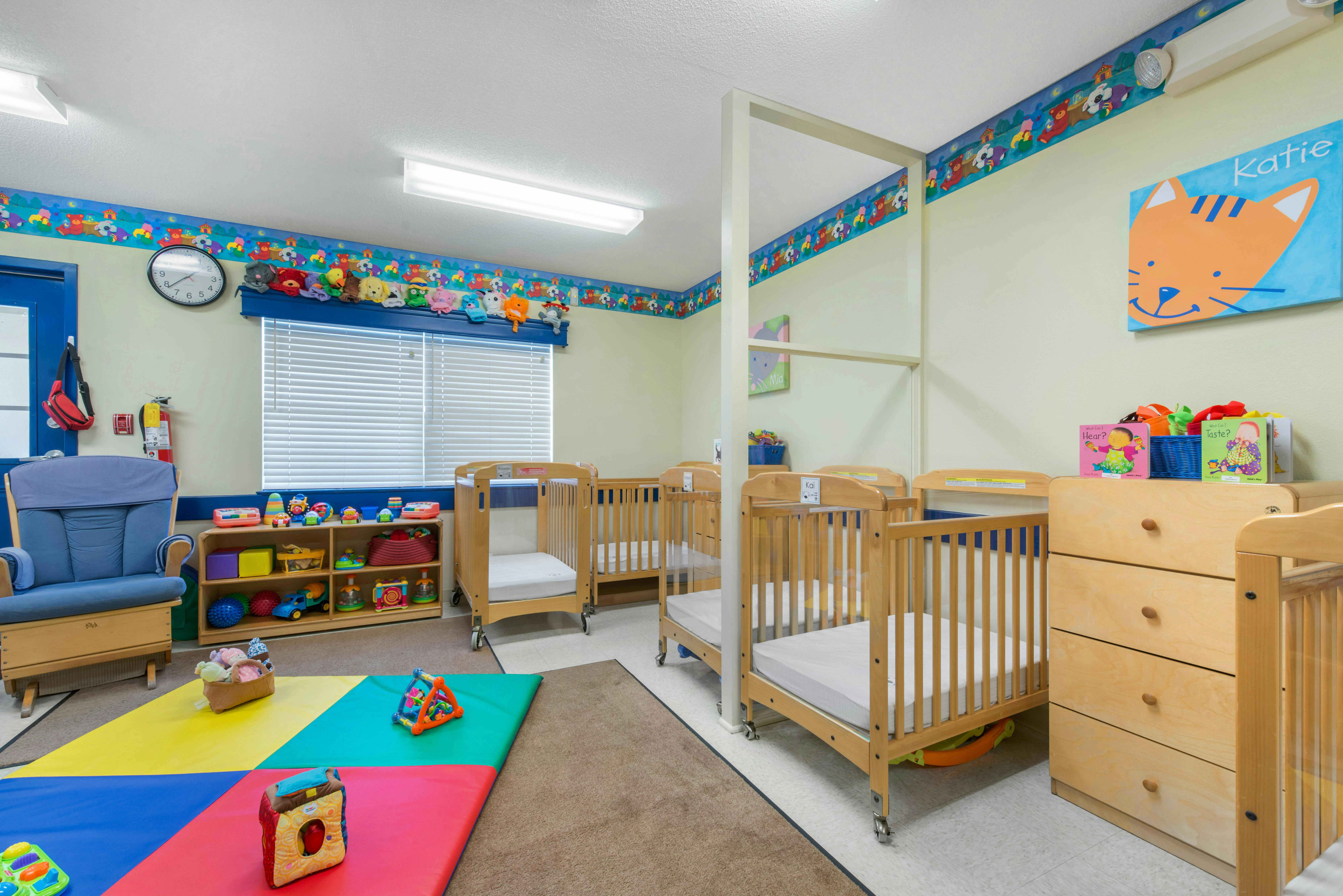 A colorful childcare room with several cribs, toys, and a rocking chair