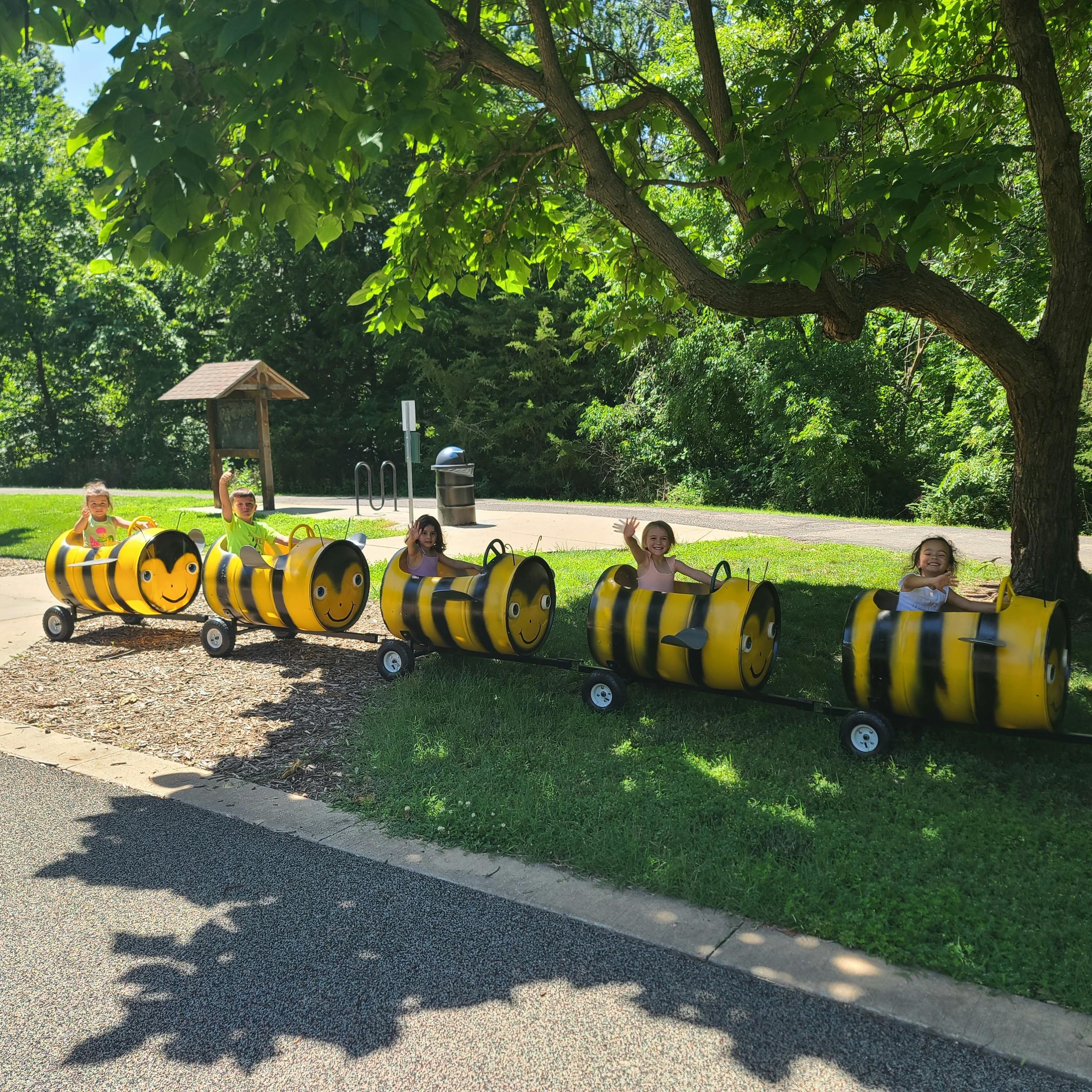 Children riding in a bee-themed barrel train outdoors
