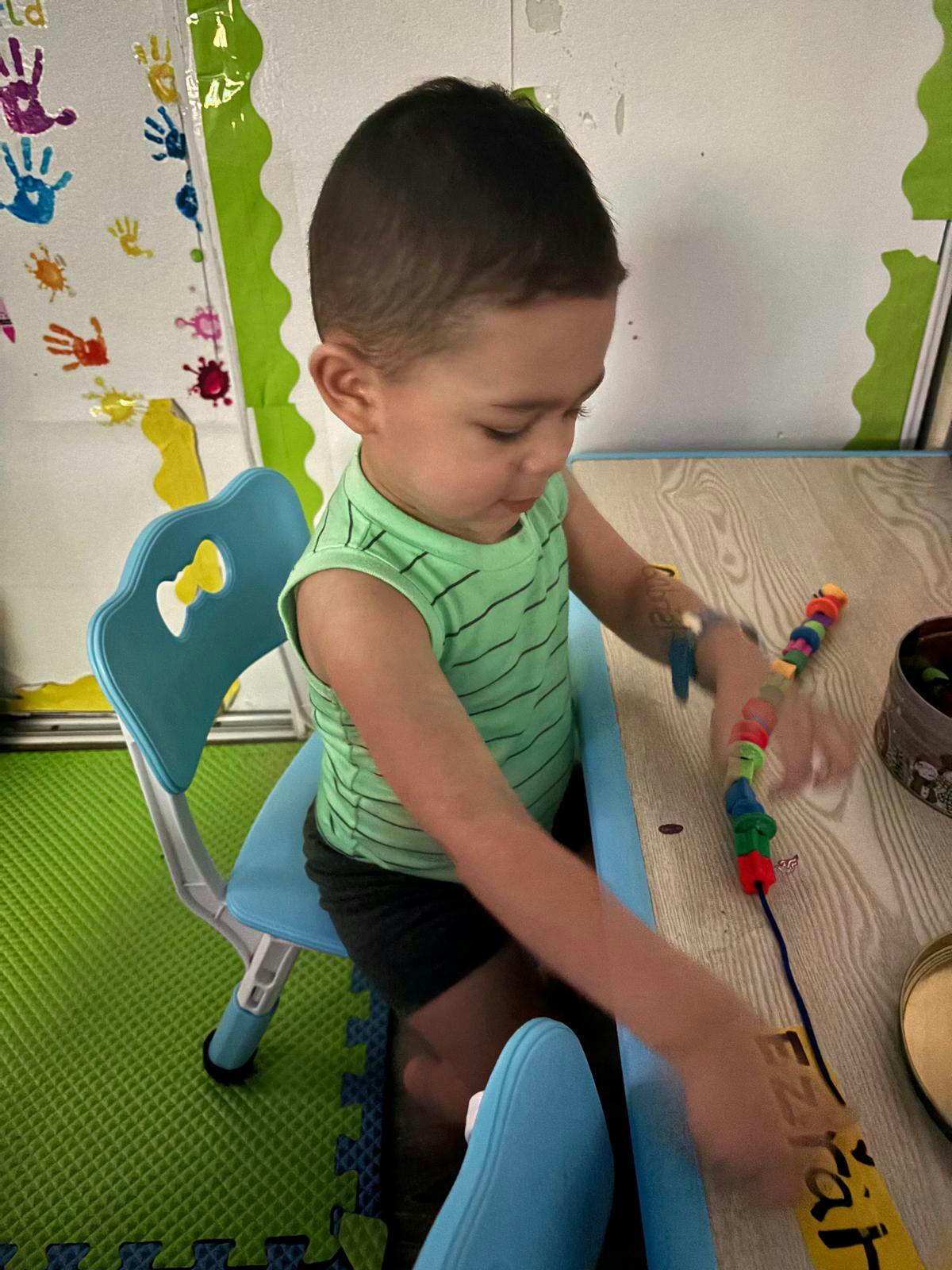 Child sitting at a desk threading small objects onto a string