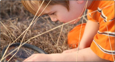 Child looking through a magnifying glass at the ground