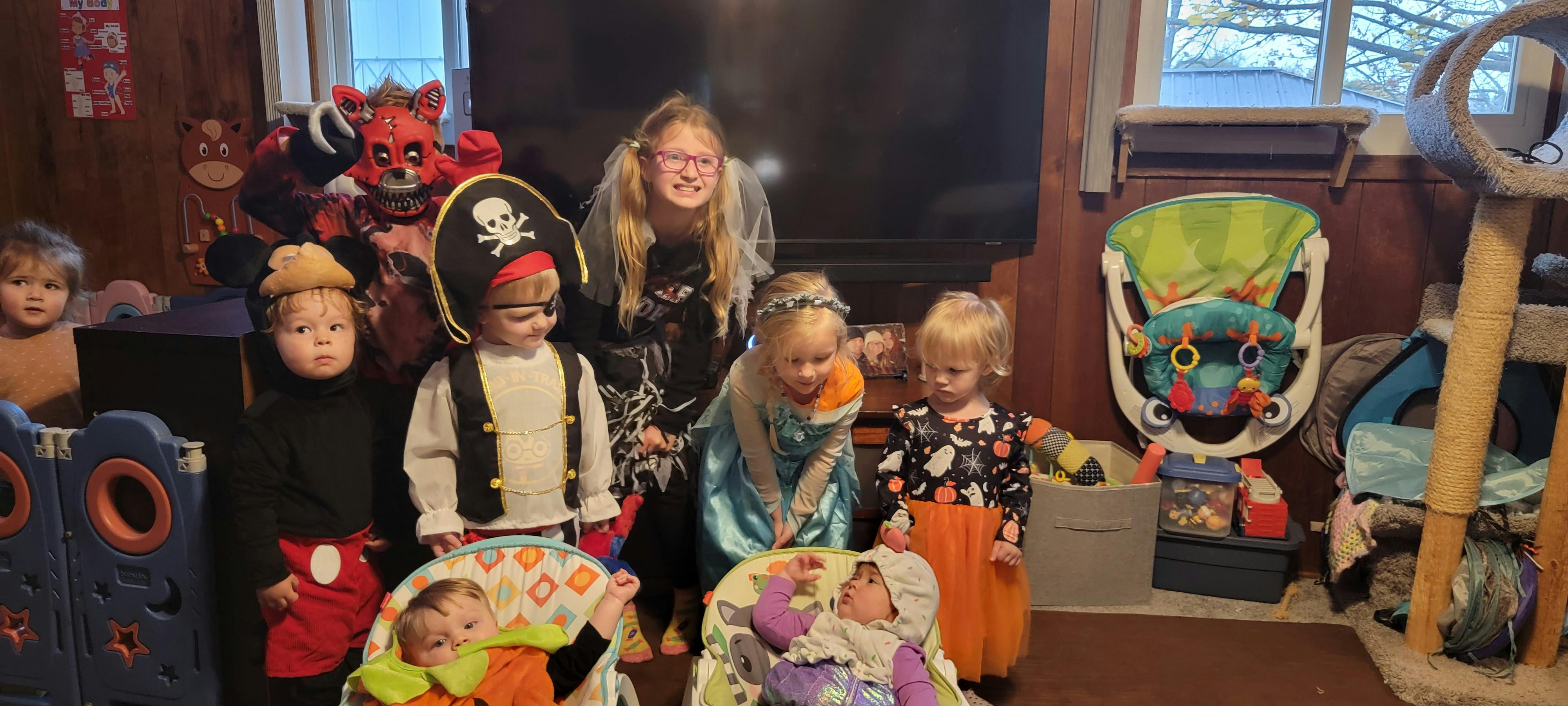 Group of children and one adult in costumes, with two babies in bouncers