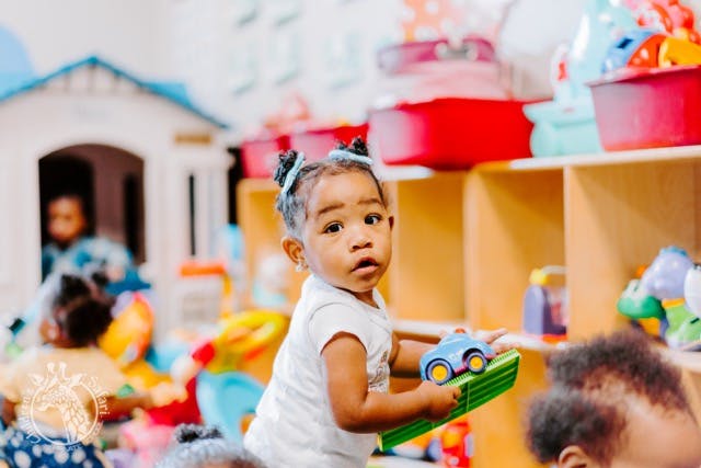 Child holding a toy car in a play area