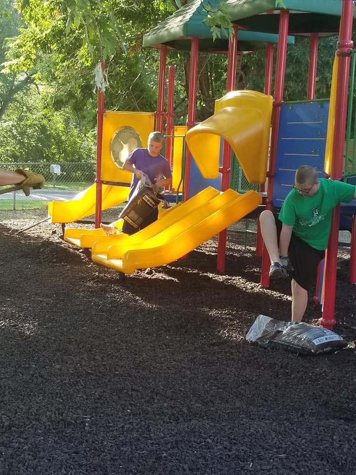 Two people on a playground structure, one holding a bag, the other adjusting a shoe