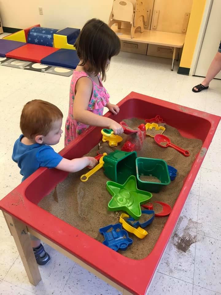 Two children playing in a sand table with toys