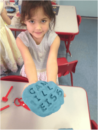Child holding blue playdough with letters impressed into it