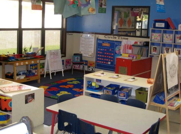 Classroom with child-sized tables and chairs, learning rug, and educational displays