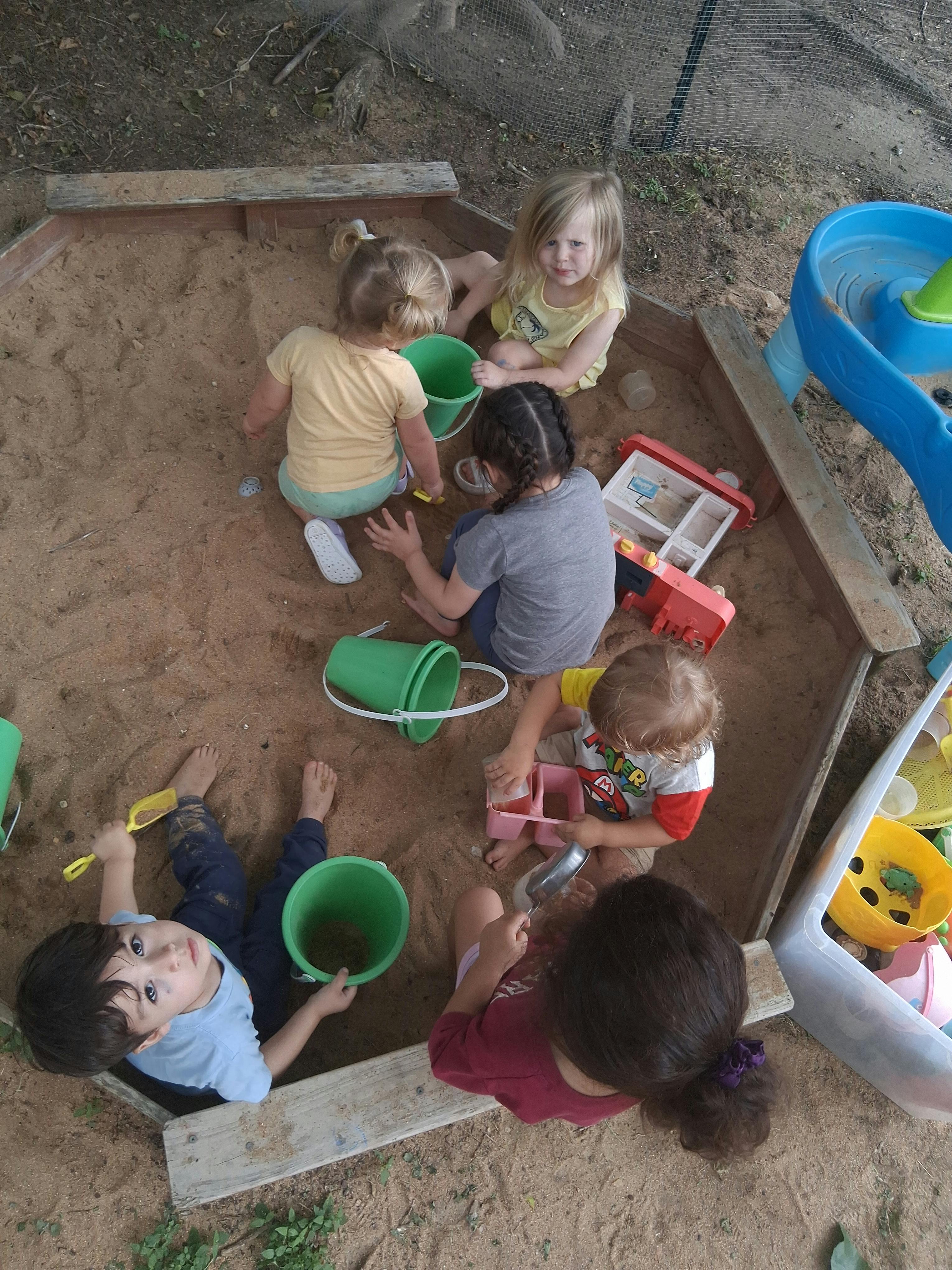 Group of children playing together with buckets and toys in a sandbox