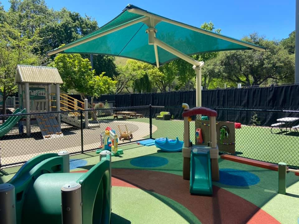 Outdoor playground with slides, play structures, and a large turquoise shade