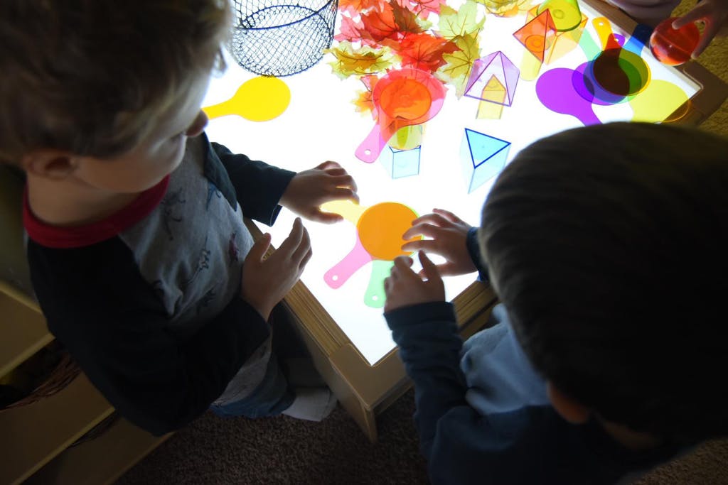 Two children playing with colorful translucent shapes on a light table