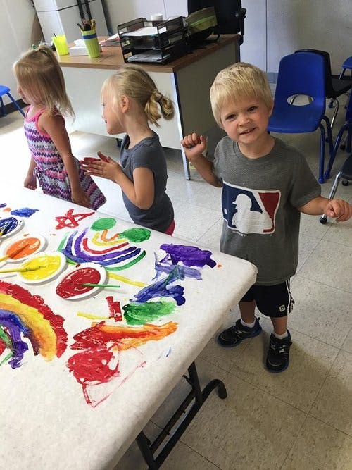 Three children standing around a table covered in colorful paint