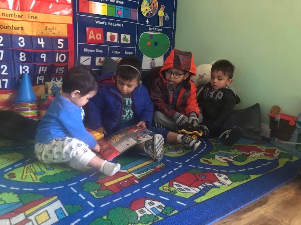 Four children sitting on a rug, looking at a book