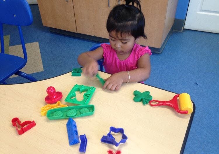 Child playing with colorful playdough and cookie cutters at a table