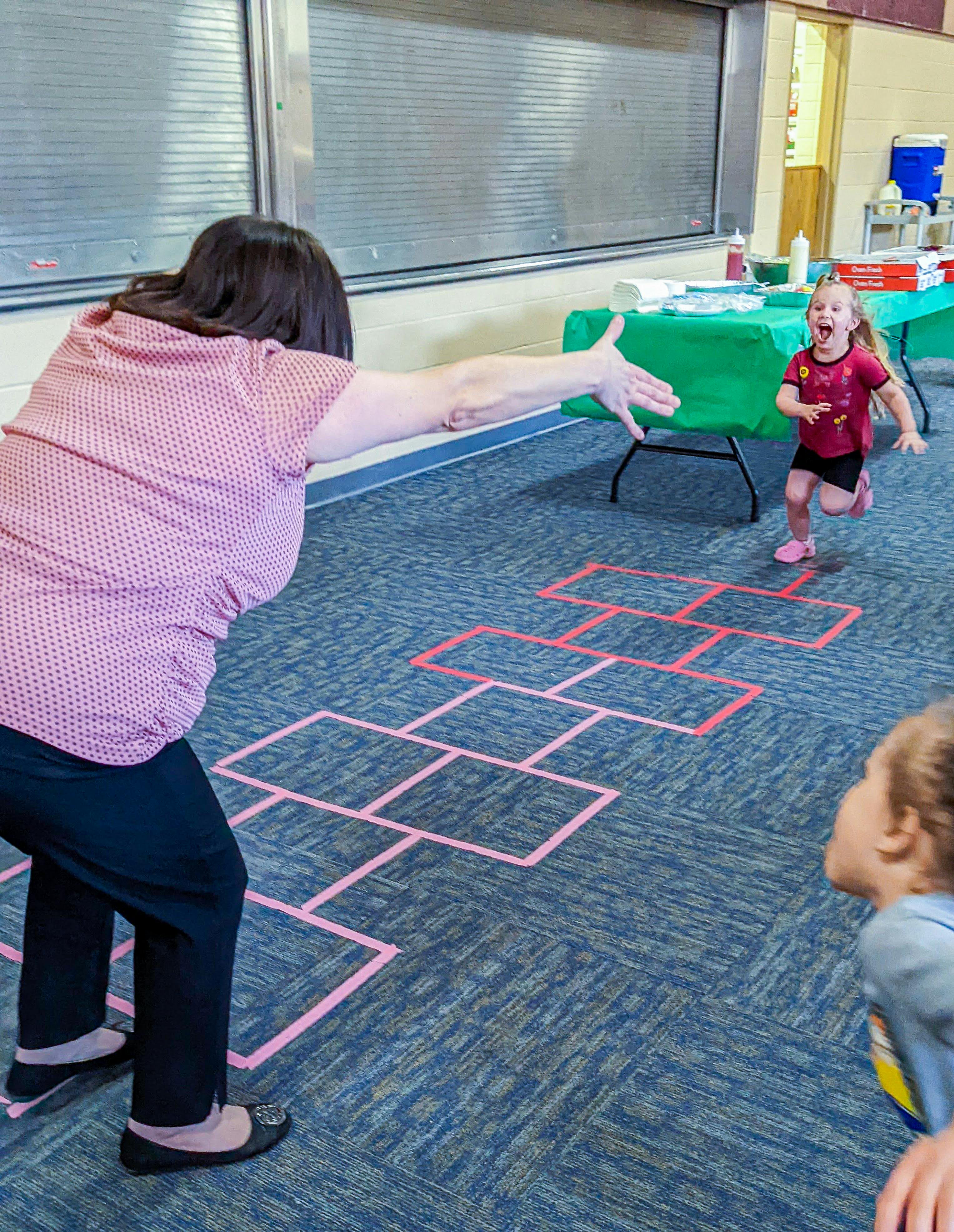 Person reaching out to a child running on a hopscotch grid