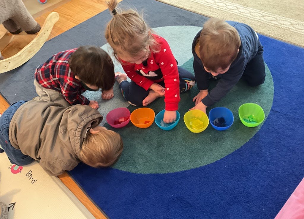 Four children playing with colorful bowls on a blue and green rug