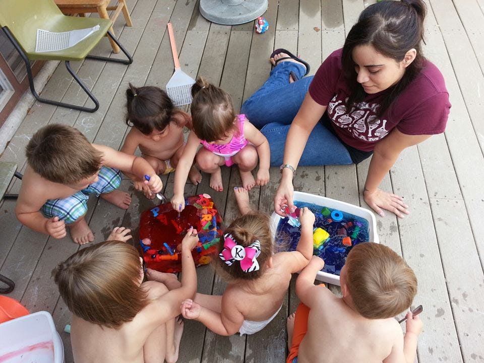 Adult and multiple children playing with toys on a wooden deck