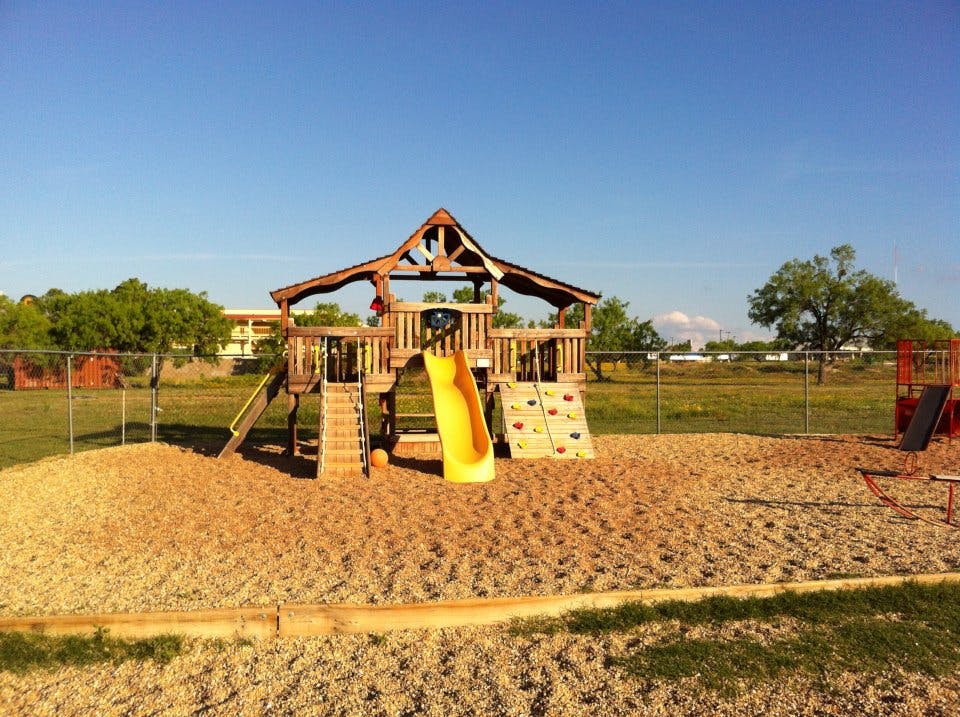 Wooden playground structure with a yellow slide on a sandy surface