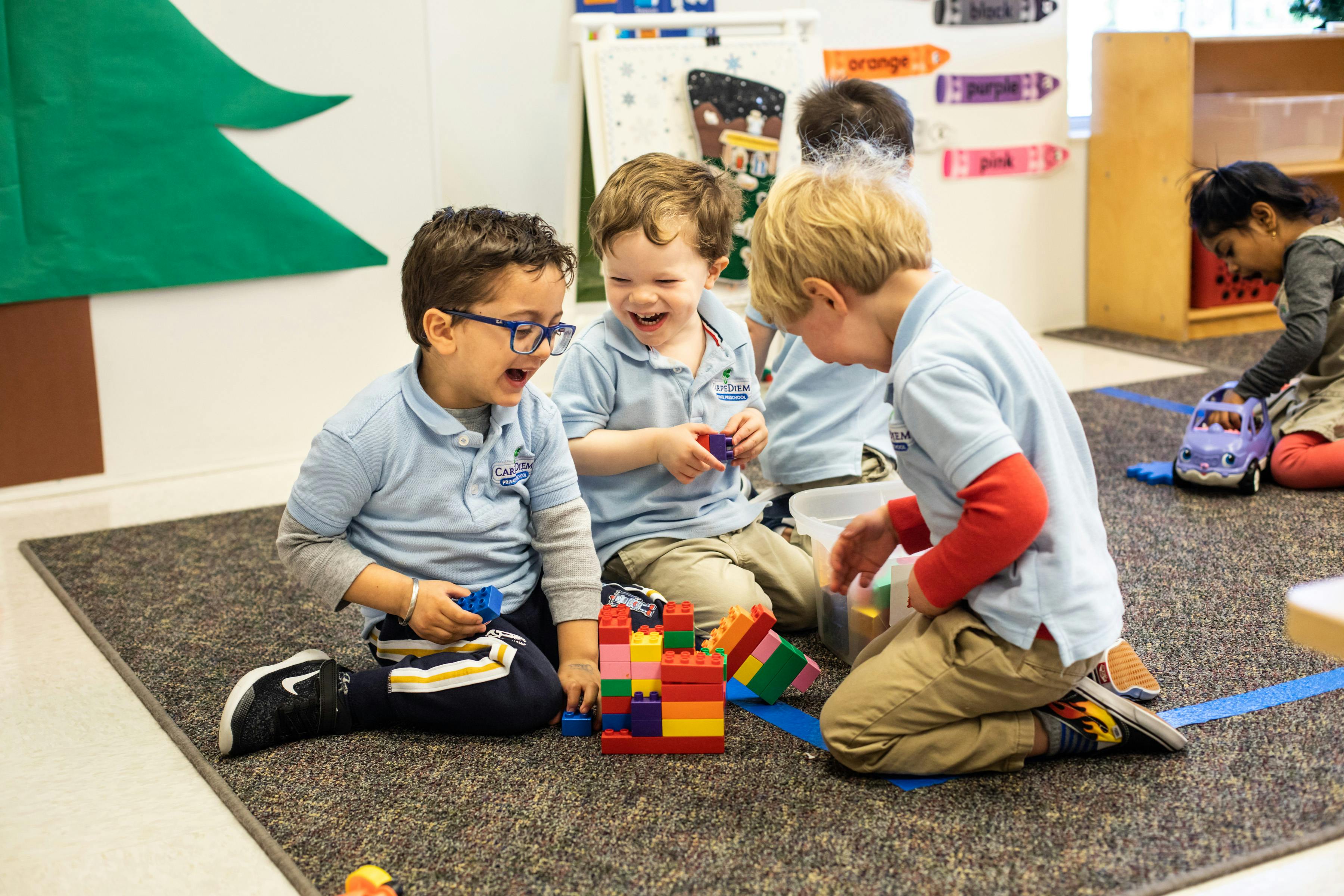 Three children playing with building blocks on a rug in a classroom