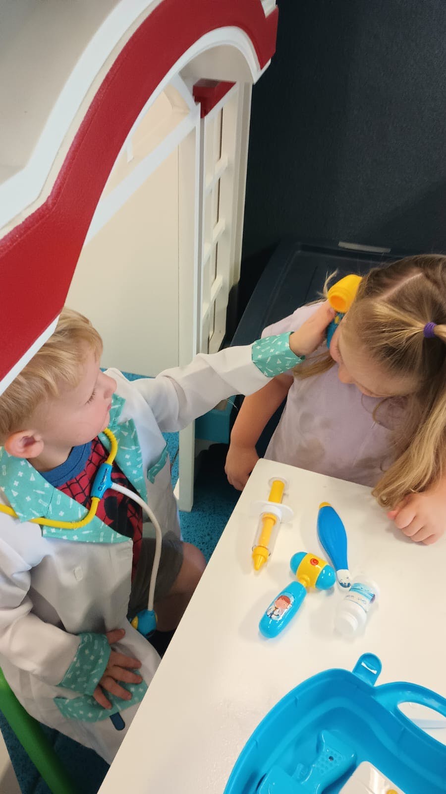 Child in doctor costume examining another child with a toy stethoscope