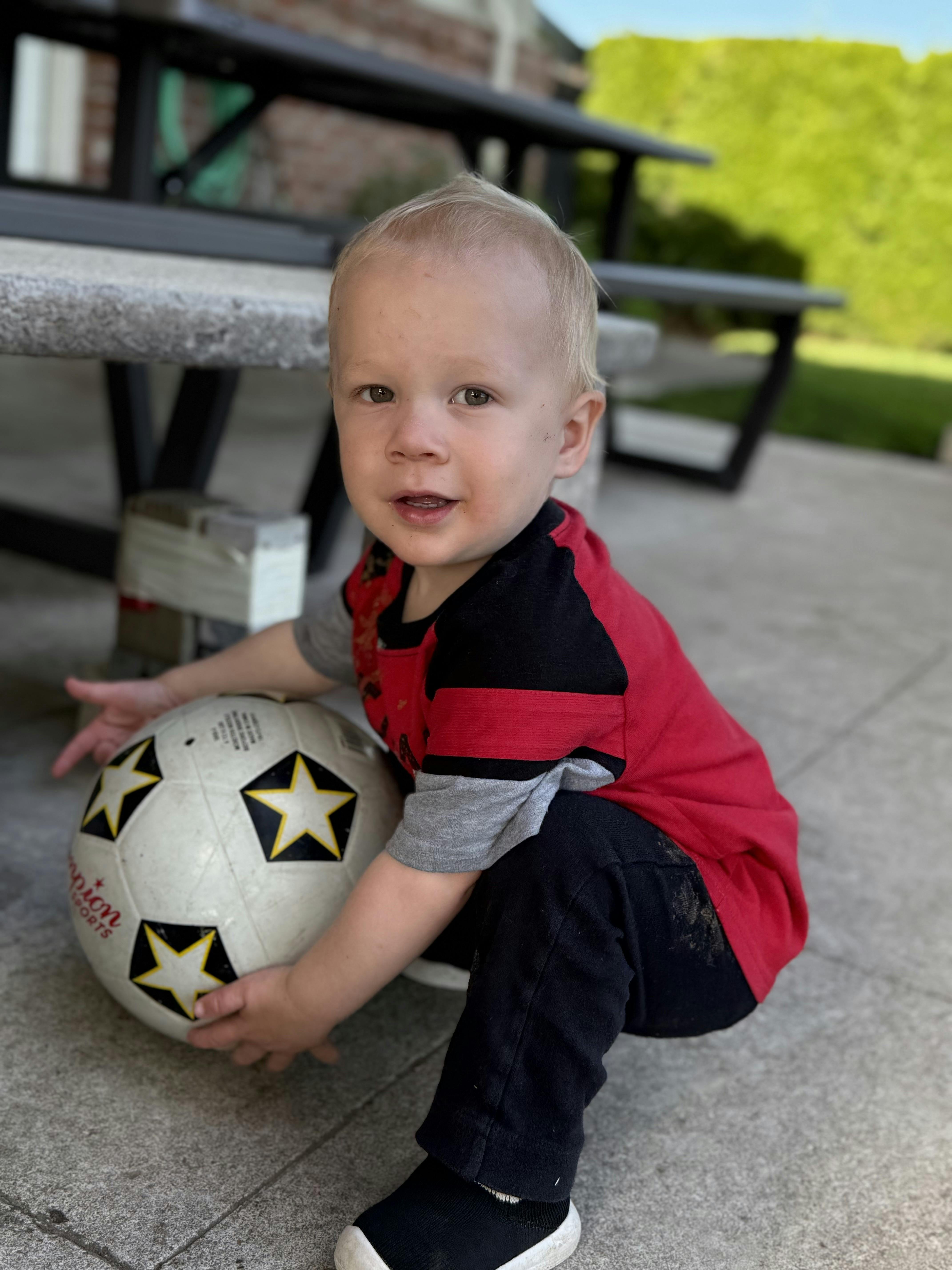 Child crouching and holding a soccer ball on a patio
