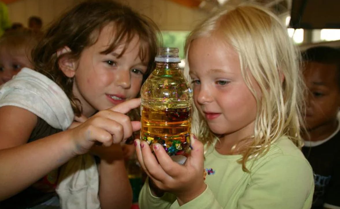 Two children looking at a bottle with liquid and objects inside