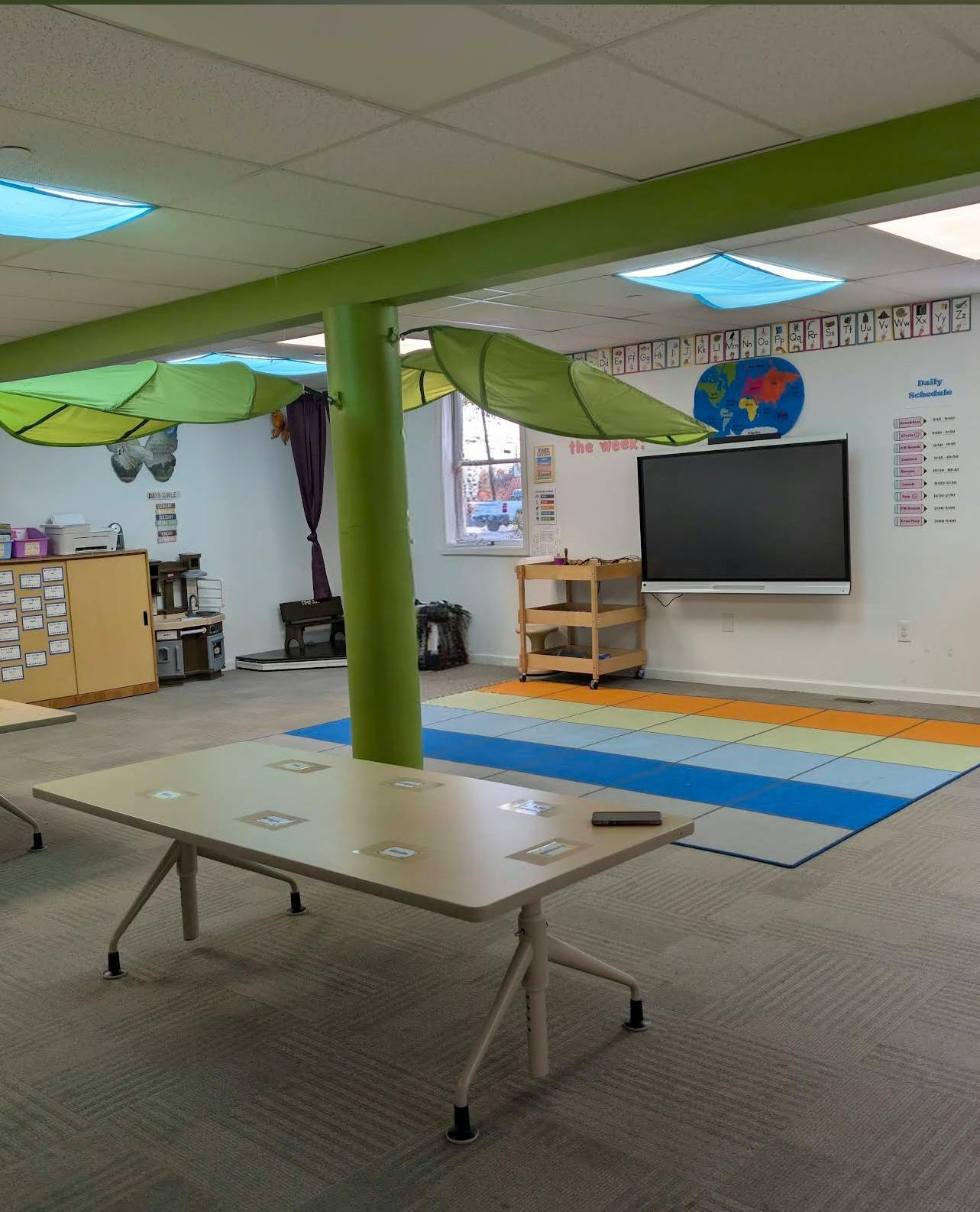 Classroom with tables, an interactive board, and a colorful mat