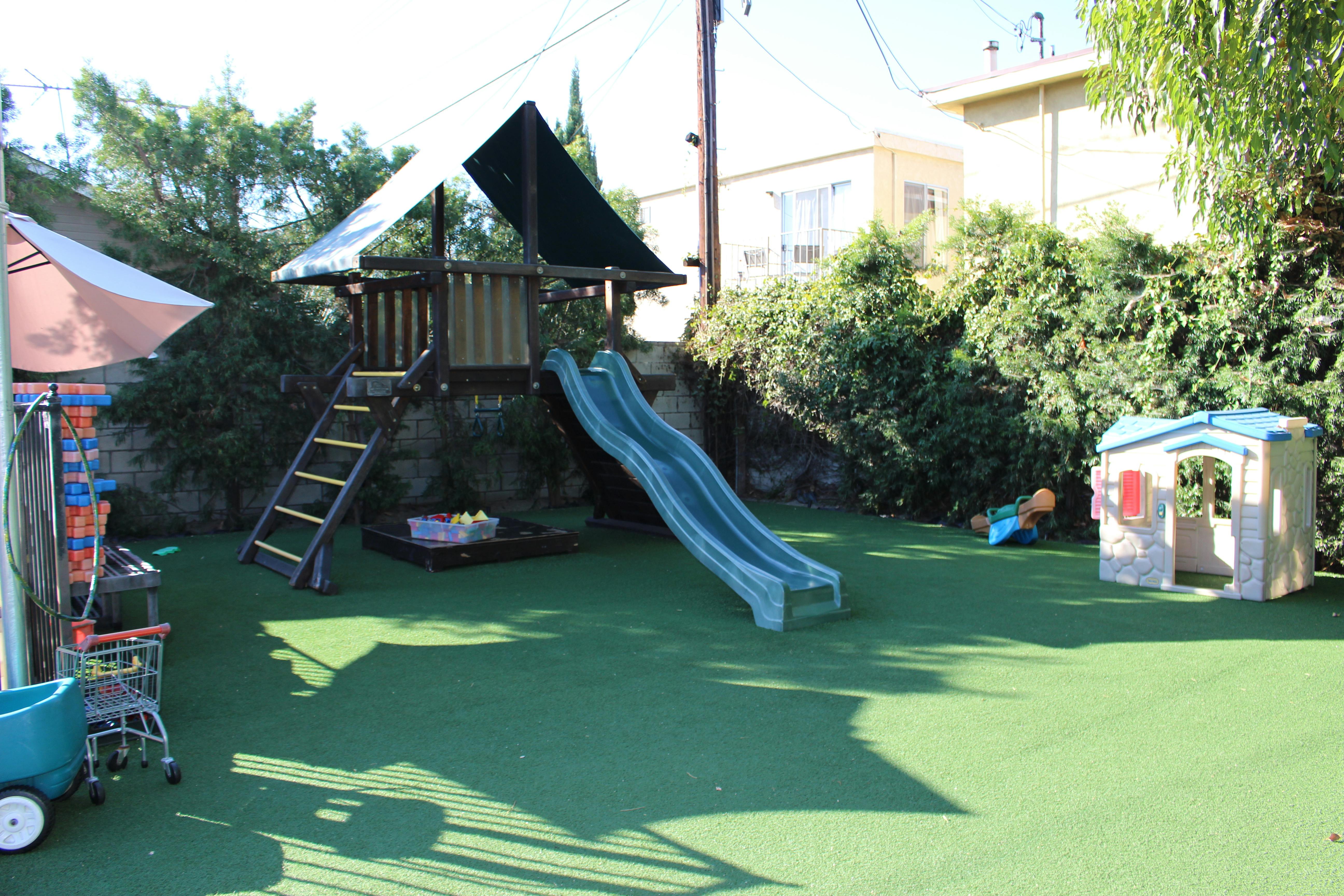 Playground with a wooden play structure, slide, and small playhouse on artificial turf