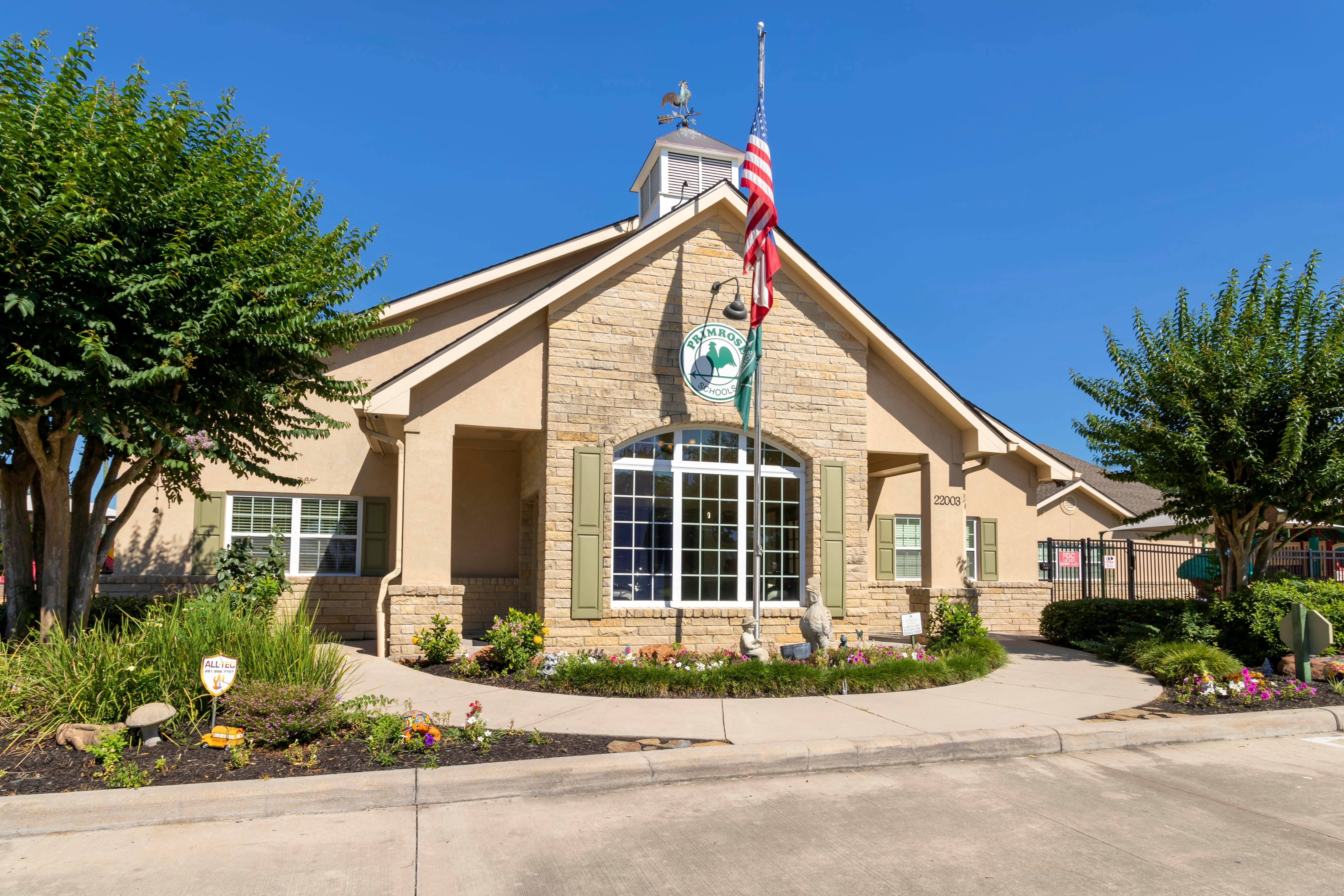 A tan and stone building with a large arched window, a flag, and a weather vane