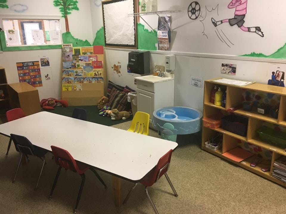 Classroom with a long white table and chairs, shelves, and wall drawings