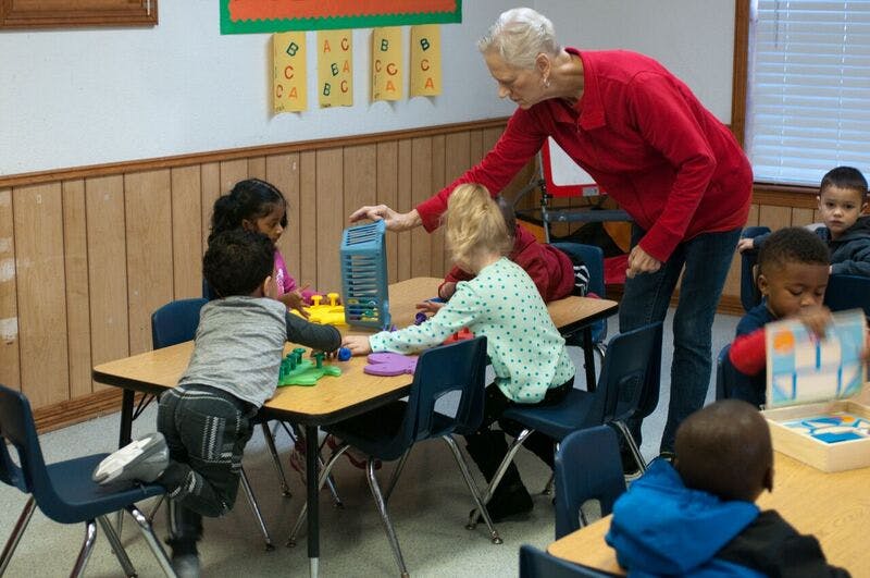 Adult helping children play with toys at a table in a classroom