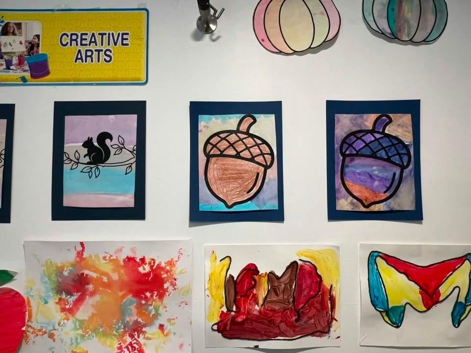 Children art display on a wall featuring drawings of acorns and abstract paintings