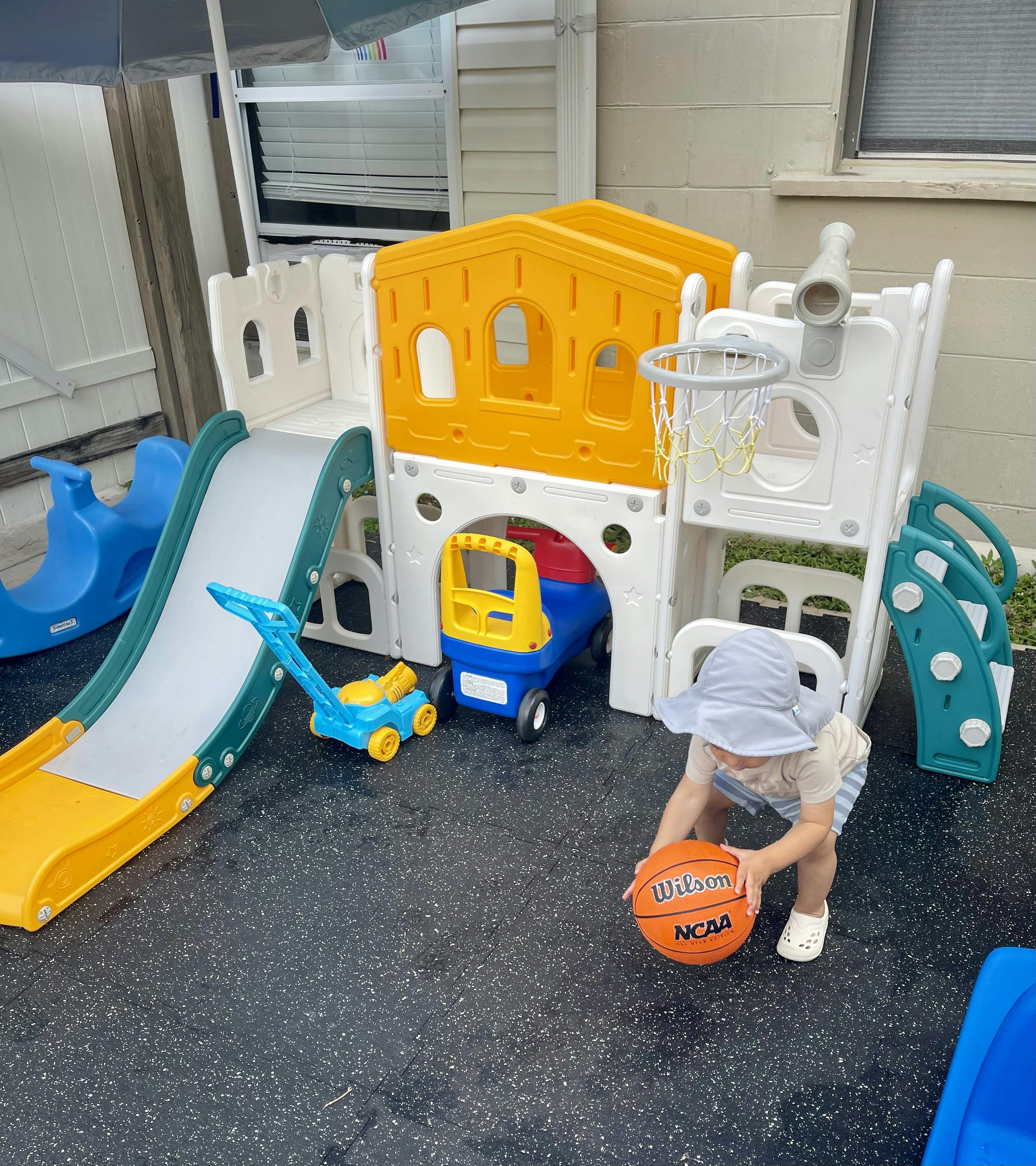 Child holding a basketball in front of a plastic play structure