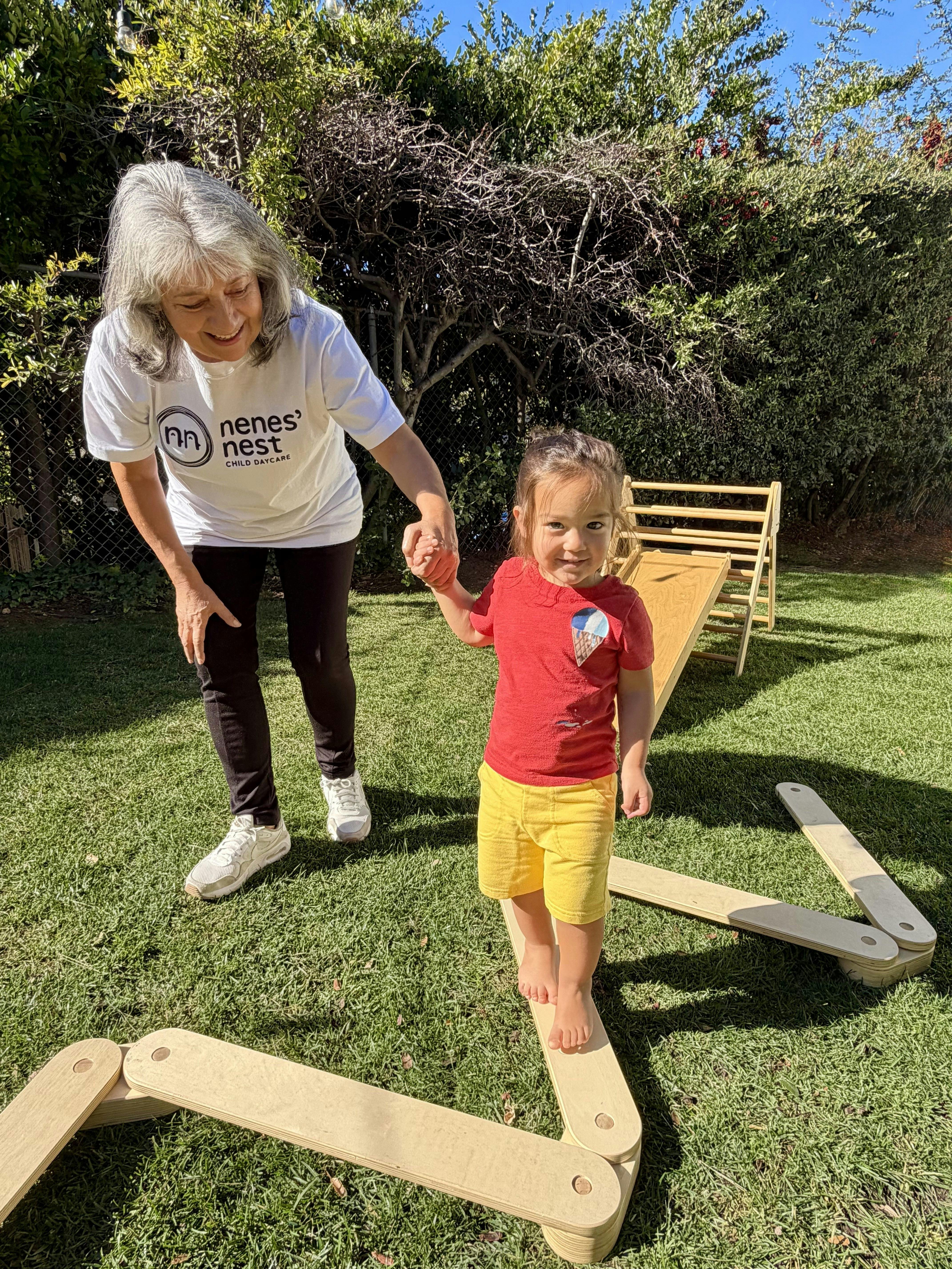 Person holding a child's hand as the child balances on wooden planks