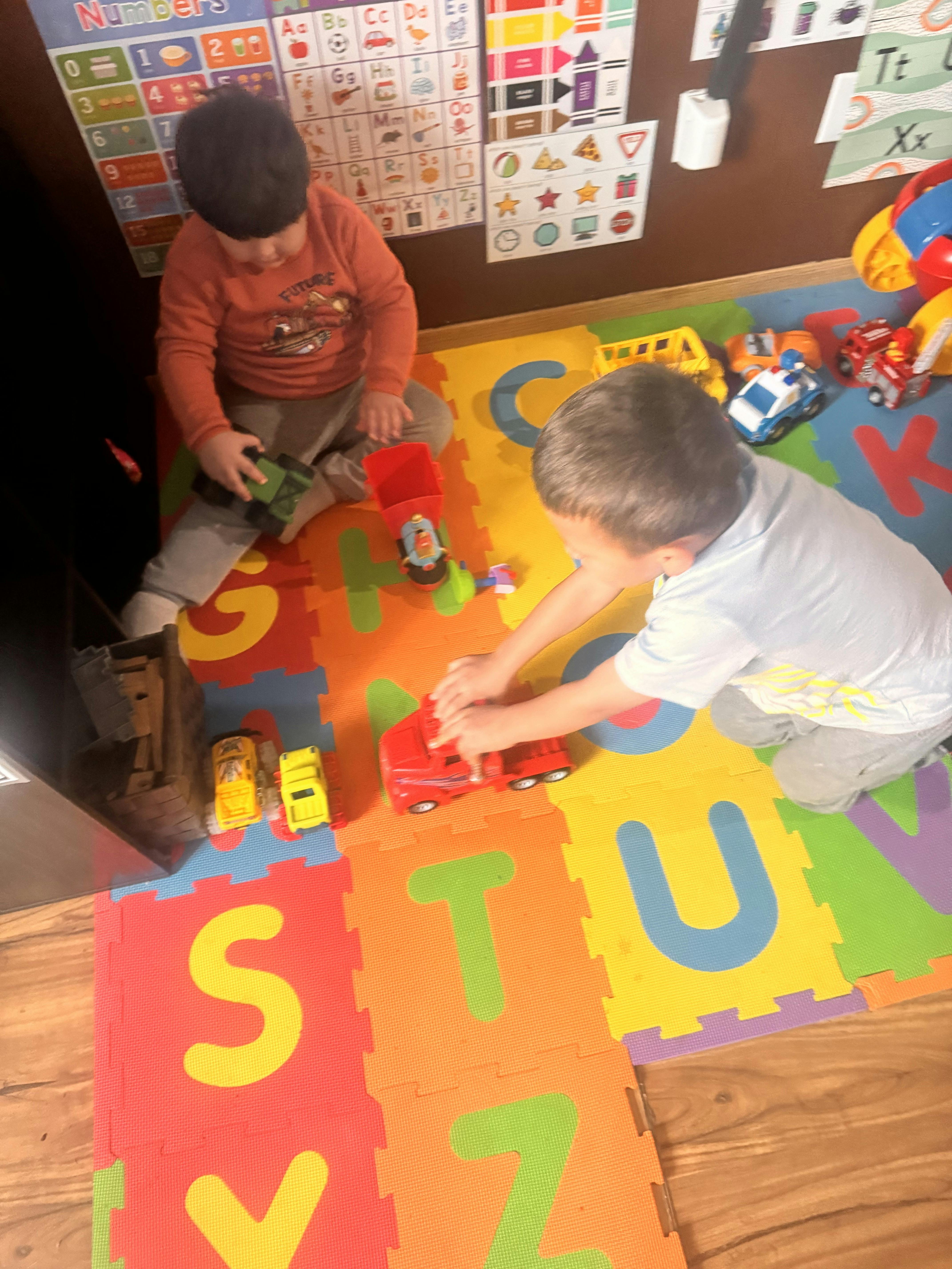 Two children playing with toy trucks on an alphabet mat