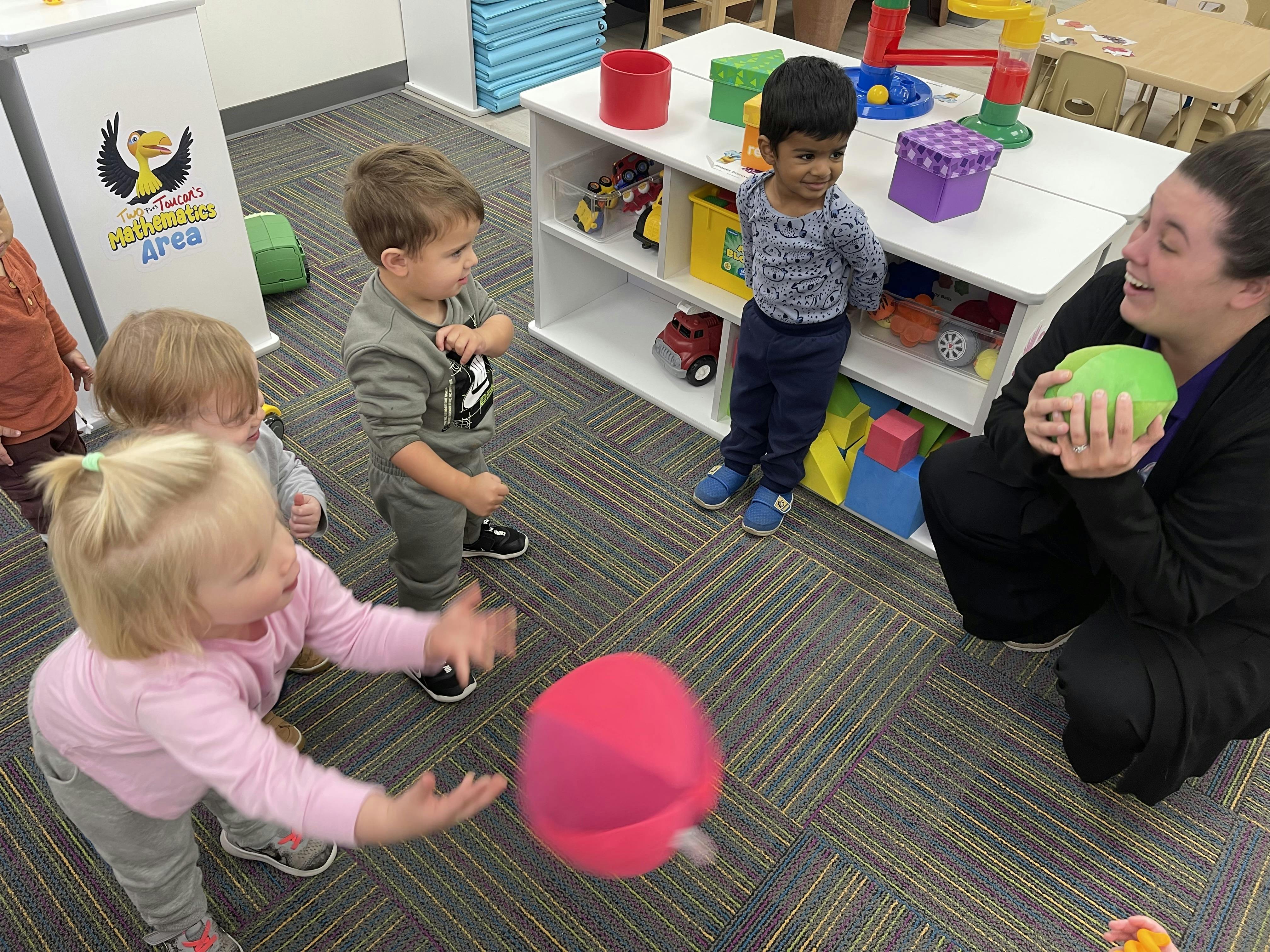 Adult and children playing with balls in a classroom