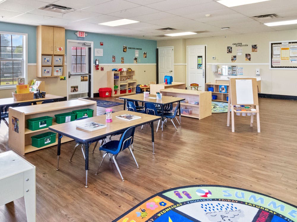 An empty early childhood classroom with small tables, chairs, and learning materials