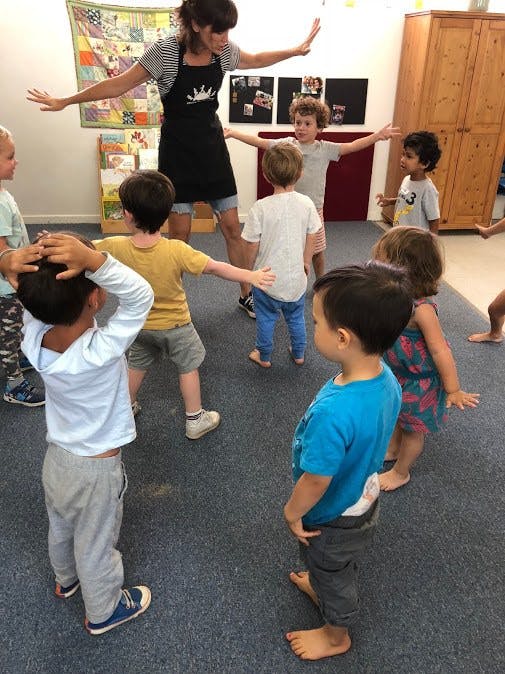 Adult and children in a classroom with arms outstretched