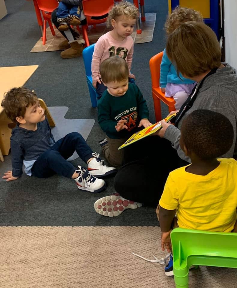 Adult reading a book to several children in a classroom