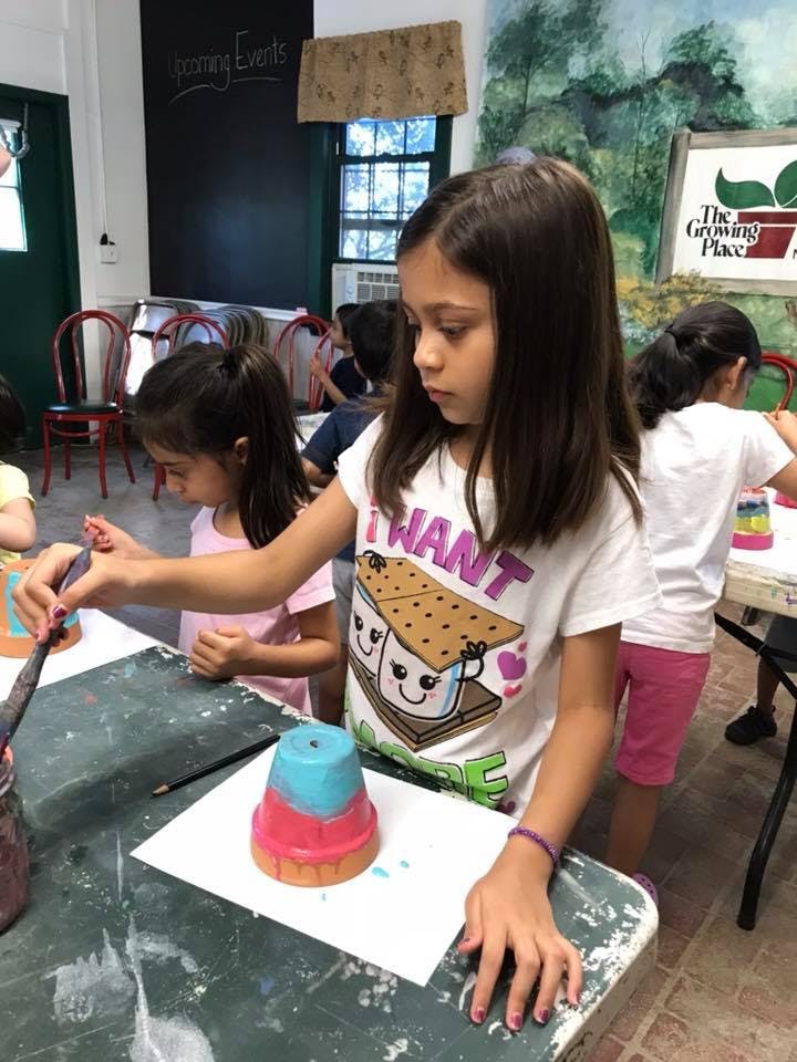 Child painting a small pot at a table