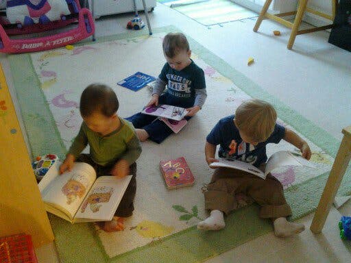 Three children sitting on a rug reading books
