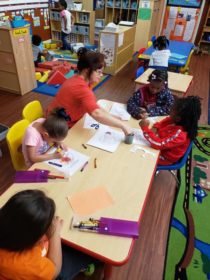 Adult and children coloring at a table in a classroom