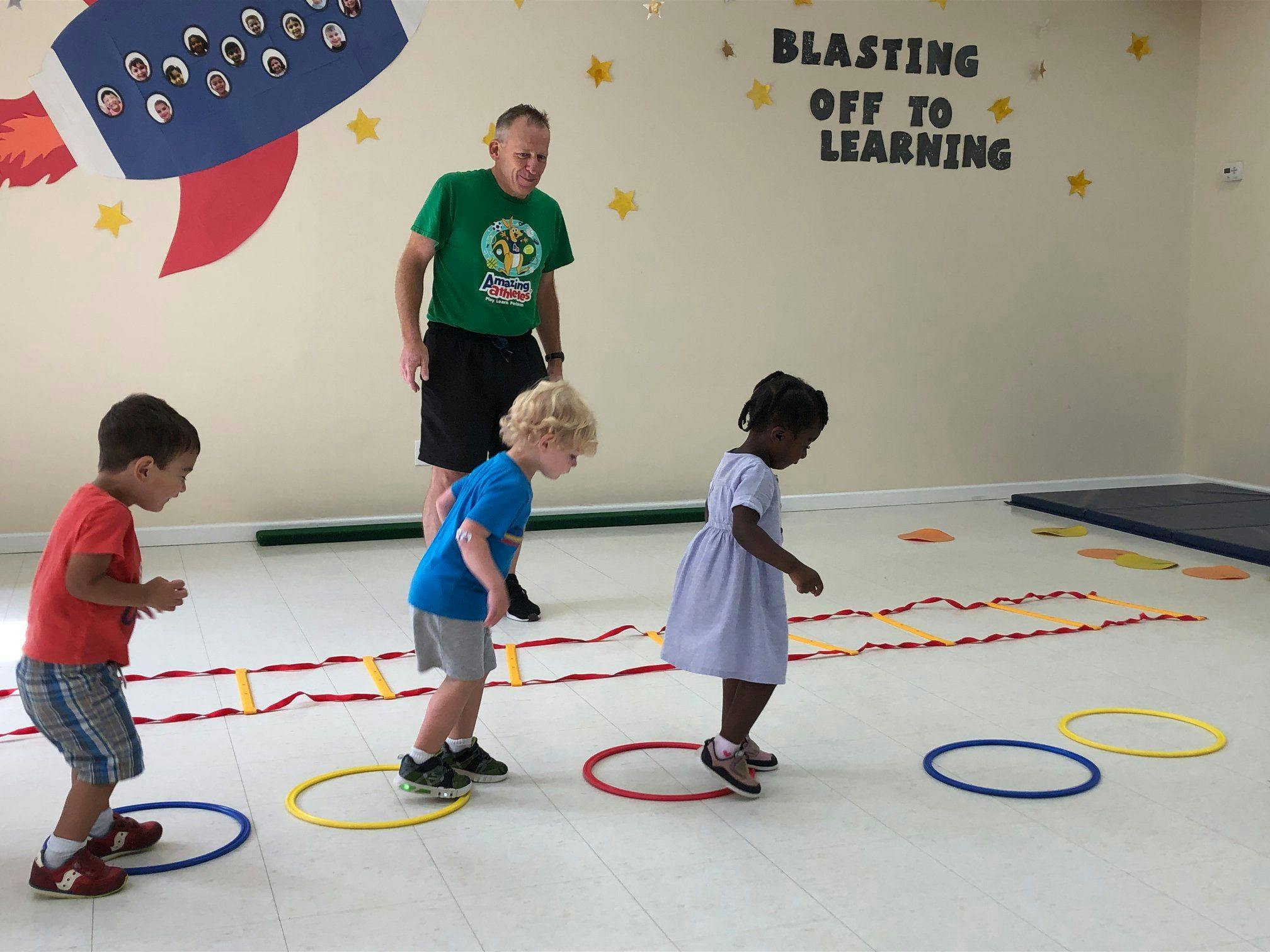 Adult supervising three children playing with hoops on the floor