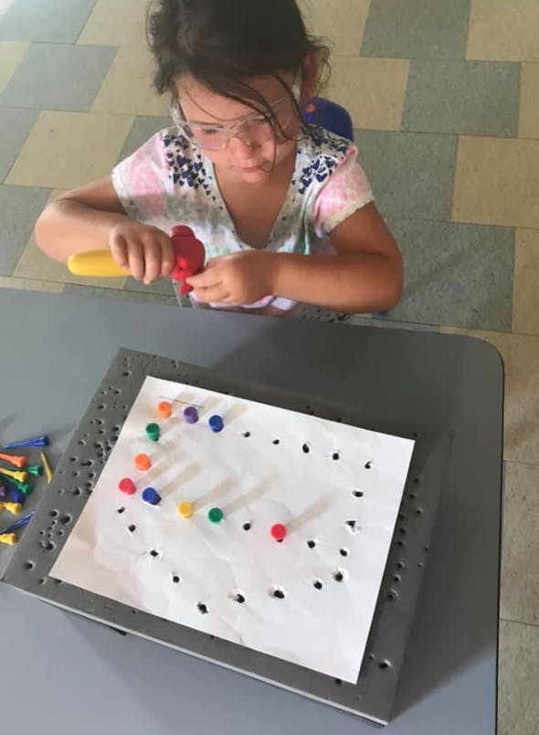 Child using a tool to place colorful pegs into a board with holes
