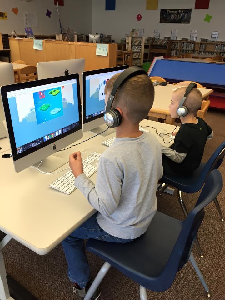 Two children wearing headphones using computers in a classroom