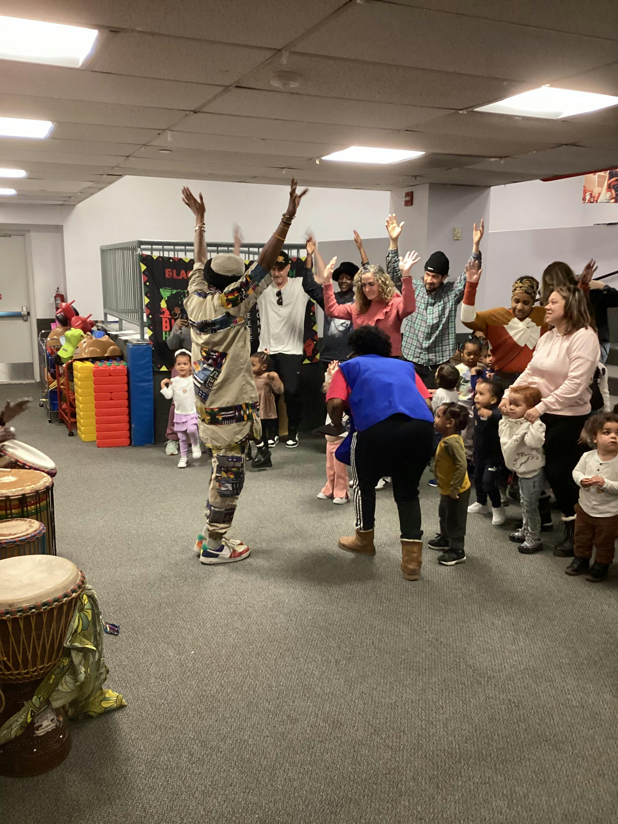People in a line dancing with their arms raised, some children