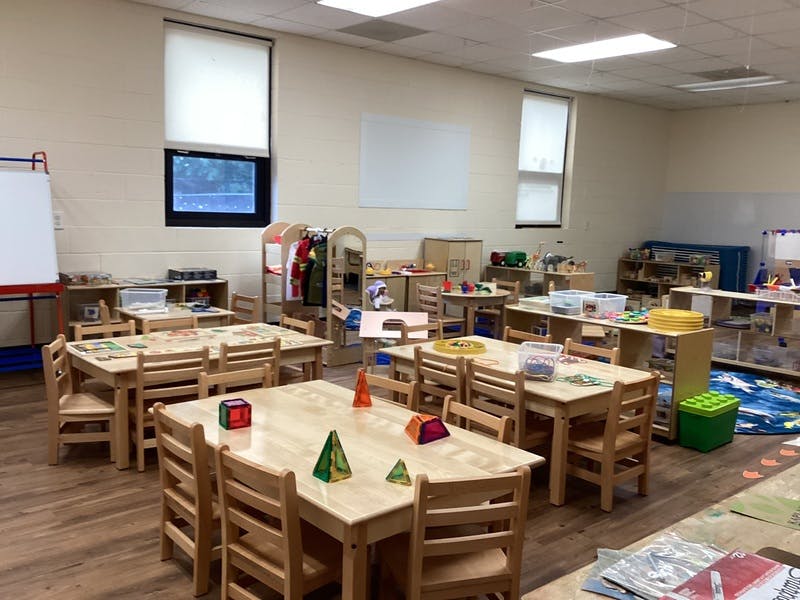Empty classroom with small wooden tables and chairs, shelves with toys