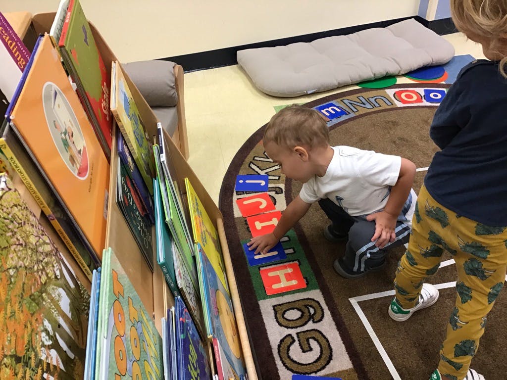 Child playing with alphabet letters on a rug in a classroom