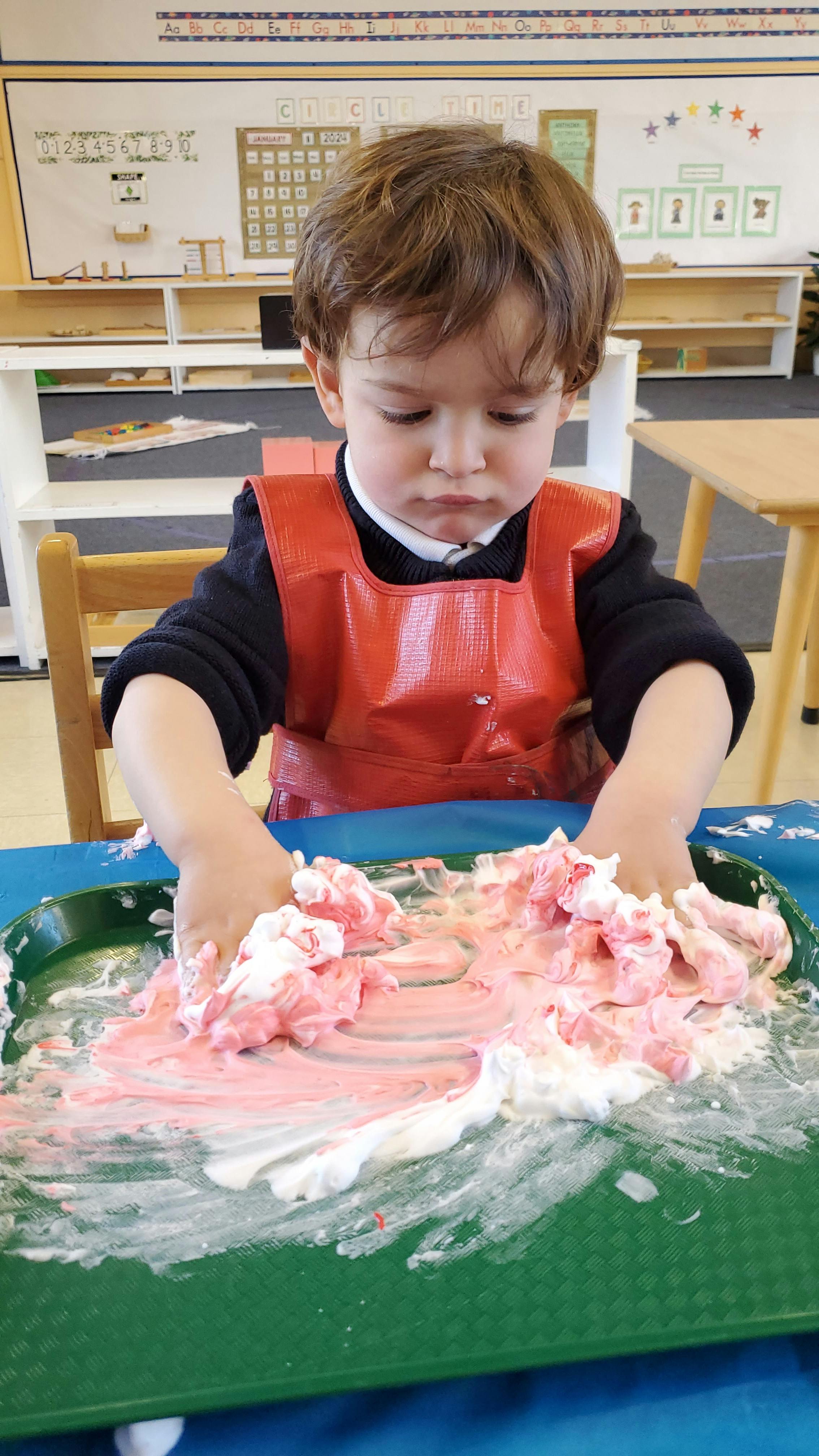 Child in a red smock playing with pink and white foam